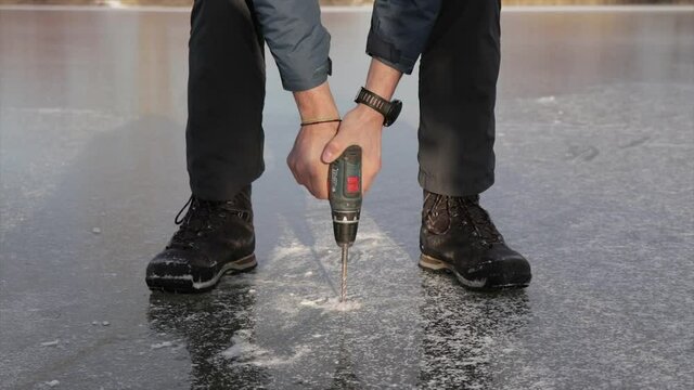 Person drilling the ice of a frozen lake with a power drill in winter. Fisherman breaking ice.