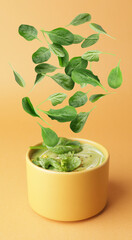 Bowl with tasty soup and falling spinach leaves on color background