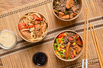 Bowls with tasty noodles and meat on wooden background