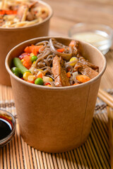 Bowls with tasty noodles and meat on wooden background