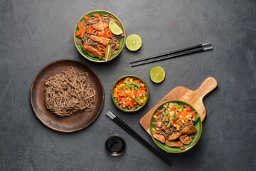 Bowls with tasty soba noodles, vegetables and meat on dark background