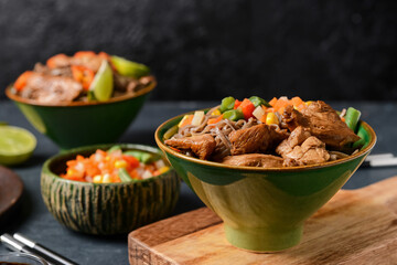 Bowls with tasty soba noodles, vegetables and meat on dark background, closeup