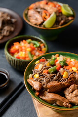 Bowls with tasty soba noodles, vegetables and meat on dark background, closeup