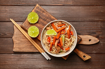 Bowl with tasty noodles and meat on wooden background