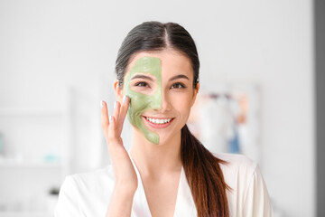 Beautiful young woman applying facial mask in bathroom, closeup