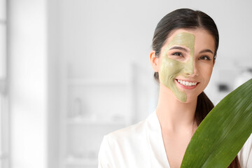 Beautiful young woman with facial mask and tropical leaf in bathroom, closeup