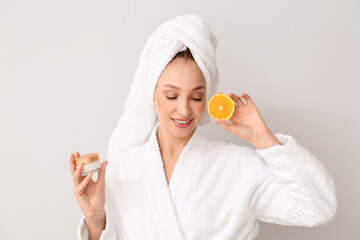Beautiful young woman with facial cream and orange on white background