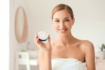 Beautiful young woman with facial cream in bathroom, closeup
