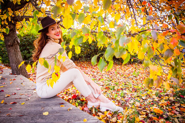 A cheerful girl in a hat is relaxing in an autumn park.