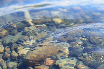 beautiful ripples on river flow over colorful stones in summer sunshine
