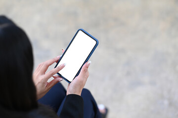 Close up view of businesswoman holding mock up smart phone with blank screen while sitting at outdoor office.