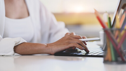 Close up view of hand of young female designer holding stylus pen and working on computer tablet.