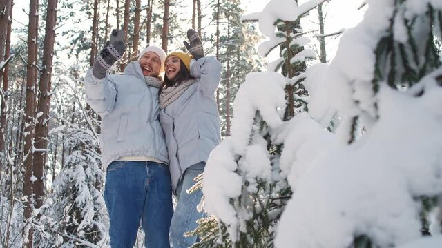 Young couple walks in a winter forest, man and female take a selfie on a smartphone against the background of a winter forest, sunny winter weather.