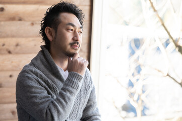 窓際で転職するか求人を見ながら悩んでいるイケメン風の日本人のヒゲ男性コピースペースあり