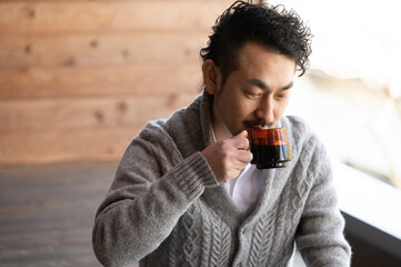 お洒落な木造の部屋でコーヒーを飲んでいる日本人男性のアップ