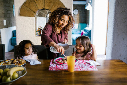 Hispanic mother serving breakfast to her daughters at home in Latin America