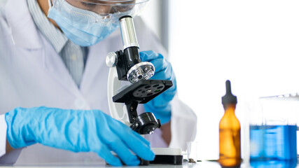 Fototapeta premium Young Asian scientist Working looking through a microscope doing research for analyzing a Experiments sample in a forensic laboratory.