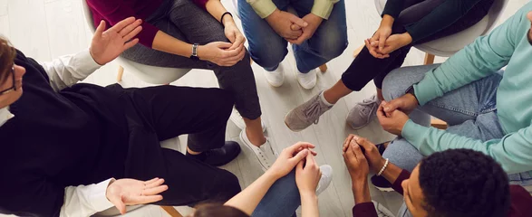 Poster Top view of diverse people sitting in a close circle and talking to a therapist. Cropped image of unidentified people receive help and support during a group therapy session. Concept of group therapy. © Studio Romantic