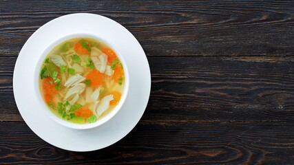 Bowl of chicken soup on a brown wooden table with copy space. Top view.