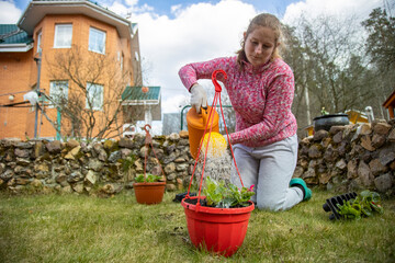 woman watering potted flowers from a garden watering can in the backyard of a house in spring