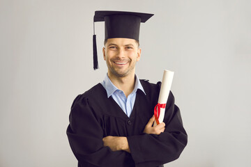 Studio portrait of satisfied student with his graduation certificate. Happy academy, college or university graduate standing against gray background, holding his diploma scroll and smiling at camera - obrazy, fototapety, plakaty