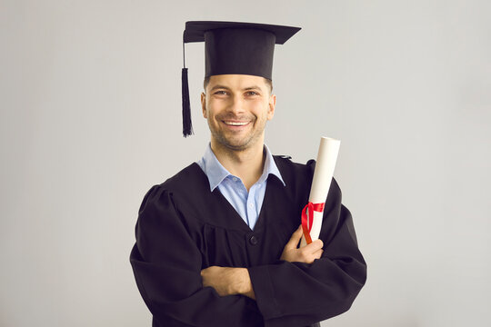 Studio Portrait Of Satisfied Student With His Graduation Certificate. Happy Academy, College Or University Graduate Standing Against Gray Background, Holding His Diploma Scroll And Smiling At Camera