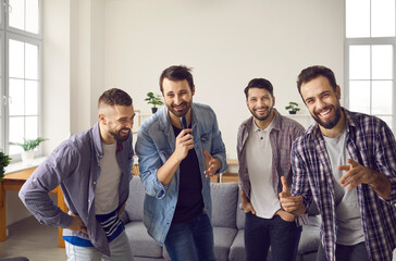 Positive cheerful male friends singing favourite songs on karaoke microphone together during home...