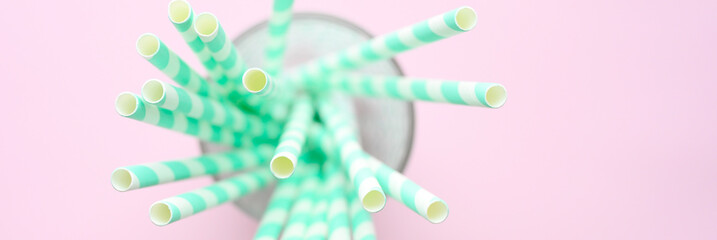 blurred pile of paper striped white and green drinking straws for party in clear glass small bottle on pink background. space for text. banner