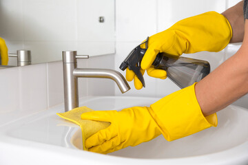 Yellow gloves cleaning sink in the bathroom. Disinfecting the bathroom. Prevention of coronavirus infection.