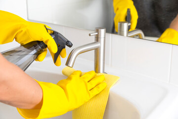 Yellow gloves cleaning sink in the bathroom. Disinfecting the bathroom. Prevention of coronavirus infection.