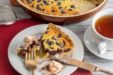 Fresh slice of cherry pie with ice cream and white cup with tea on a wooden background
