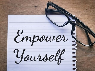 Phrase EMPOWER YOURSELF written on a piece of paper with eye glasses. Motivational quote.