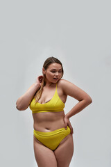 Curious curvy young female model wearing yellow underwear looking away while posing isolated over light background