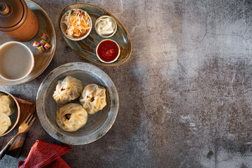 Buuza in a plate, next to the sauce-seasoning of tomatoes with garlic, sour cream, fermented cabbage with carrots, a bowl of green tea with milk, sweets with a glass of tea leaves. 