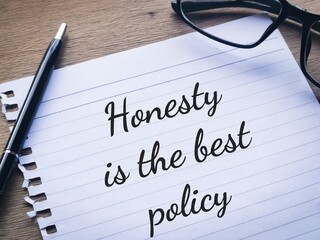 Phrase HONESTY IS THE BEST POLICY written on a piece of paper with a pen and eye glasses.