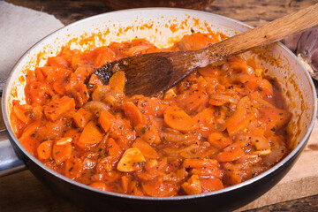 Cooking the base for soup from onions, carrots, garlic and tomatoes in a pan