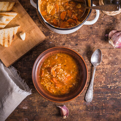 Vegetarian rice tomato soup in a plate, garlic toast and a casserole of soup on a rustic wooden table - healthy rustic lunch