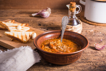 Vegetarian rice tomato soup in a plate, garlic toast and a casserole of soup on a rustic wooden table - healthy rustic lunch
