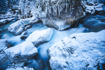 snow covered rocks in a river captured as smooth long exposure; winter landscape