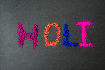 'Holi' word written by powder colors on dark background. Holi - festival of colors celebration message.
