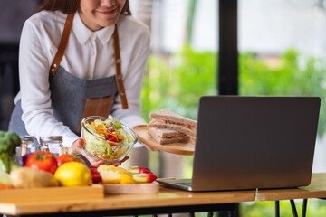 A woman videoblogger cooking and filming salad and sandwich in the kitchen, online learning cooking class concept