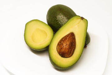 Fresh avocados with seed. Avocado cutting in half on white plate.