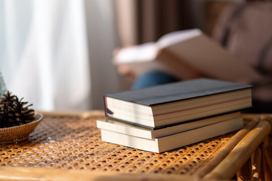 Closeup image of books on wooden table with blurred of a woman reading book in background