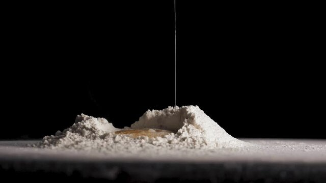 Chicken egg falls in slow motion into flour on black isolated background close up in 4K