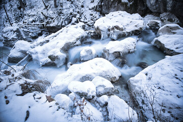 Fototapeta na wymiar snow covered rocks in a river captured as smooth long exposure; winter landscape