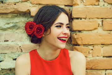 Smile teen of happy teenager girl smiling with dental braces on teeth, red lips, roses in brunette...