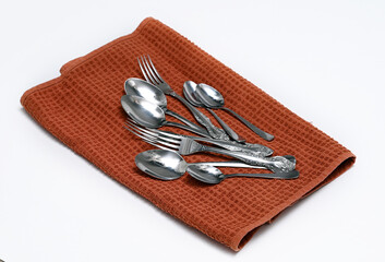 The cutlery is on a brown dish towel. Image with selective focus.