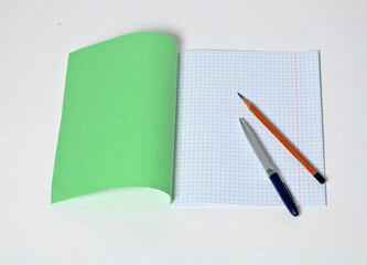 A pen and pencil lie on an open notebook. Top view.