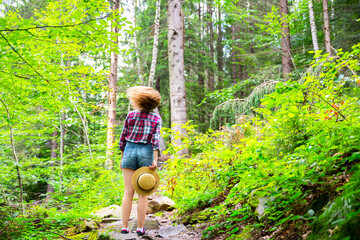 Naklejka na ściany i meble Hipster girl in the mountains. Stylish woman in straw hat and checkered shirt in forest. Wanderlust concept. Freedom and psychology concept. Beautiful nature.