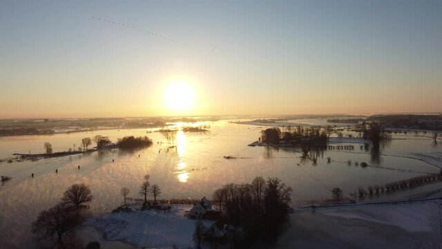 Foggy winter sunrise over the river IJssel with a high water level and ice and snow during a cold day in The Netherlands. Aerial drone point of view.